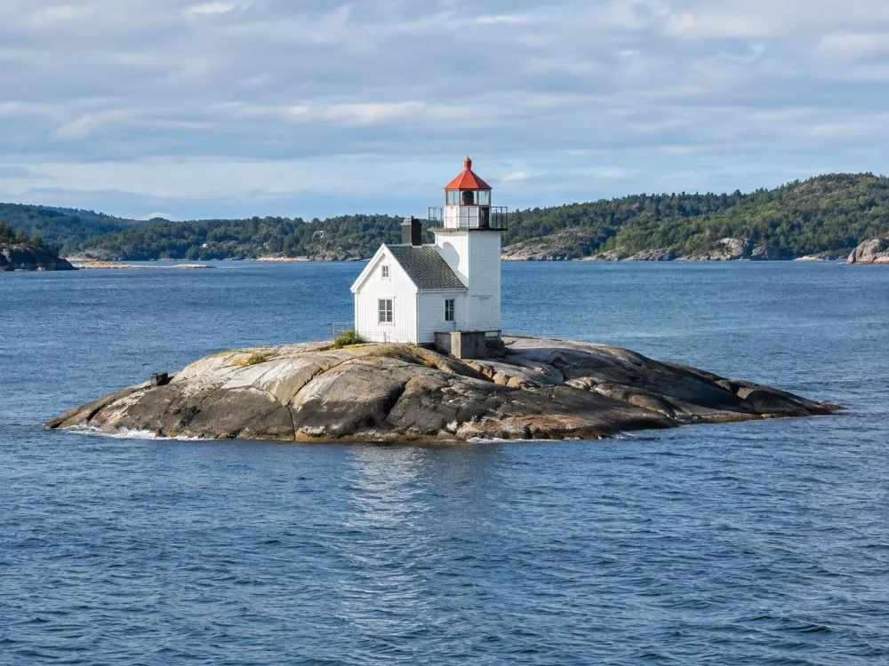 Dyna lighthouse alone on its low bare skerry in the middle of the inner harbour: a small white building on a rock barely above the water, with open fjord on every side.